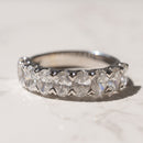 A white gold diamond eternity ring with oval-cut diamonds resting on a light marble surface.