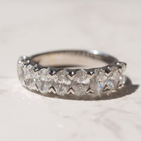 A white gold diamond eternity ring with oval-cut diamonds resting on a light marble surface.