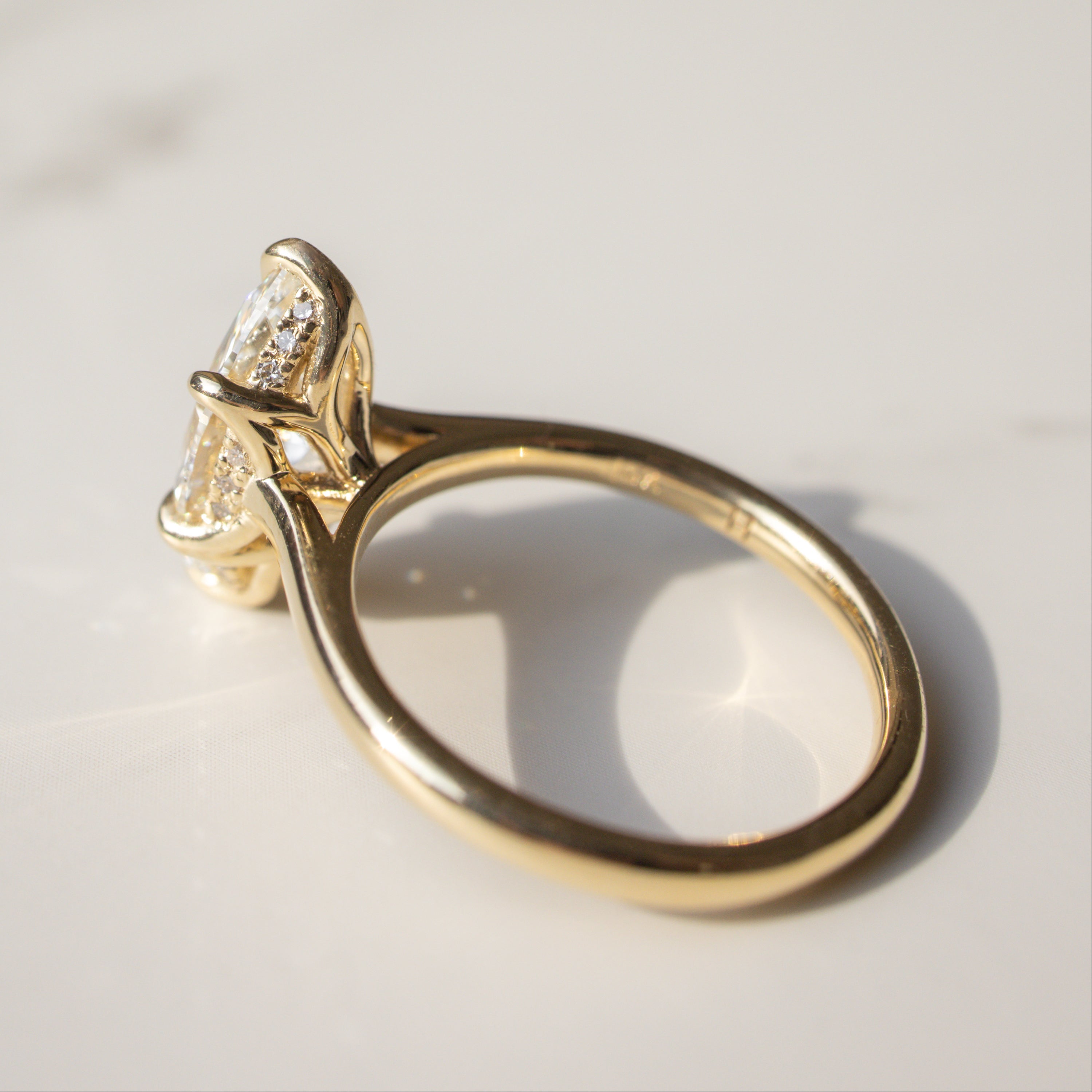 A yellow gold ring with a large marquise-cut diamond in a prong setting, resting on a light marble surface with a soft shadow.