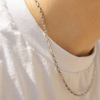 A close-up of a person's neck and upper chest wearing a silver-toned chain necklace over a white t-shirt.