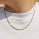 A close-up of a person wearing a silver chain necklace over a white t-shirt.