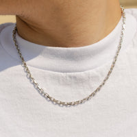 A close-up of a person wearing a silver chain necklace over a white t-shirt.