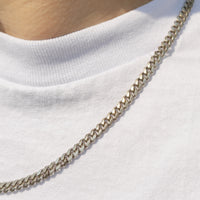 A close-up shot of a silver metal chain necklace worn around the neck over a white t-shirt.