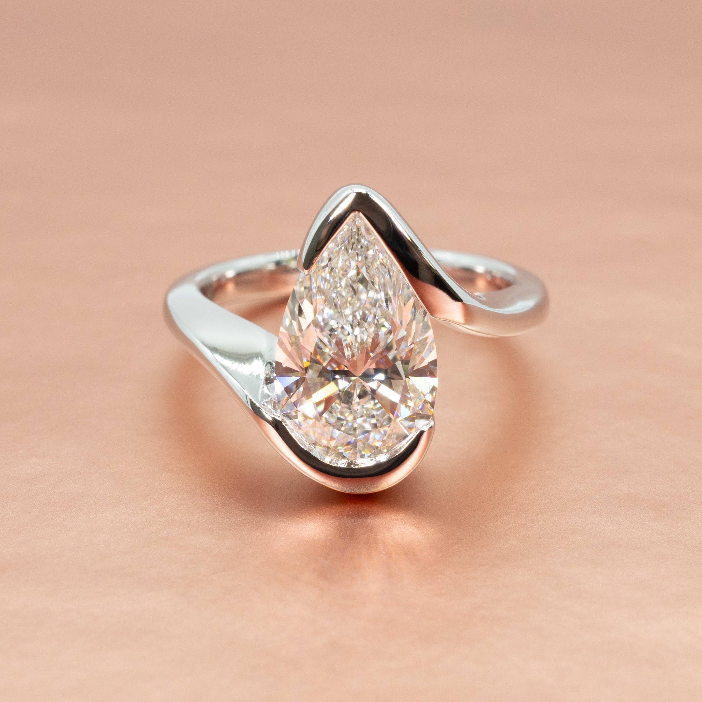 A platinum modern bypass engagement ring setting with an open, crossover shank against a rose gold backdrop