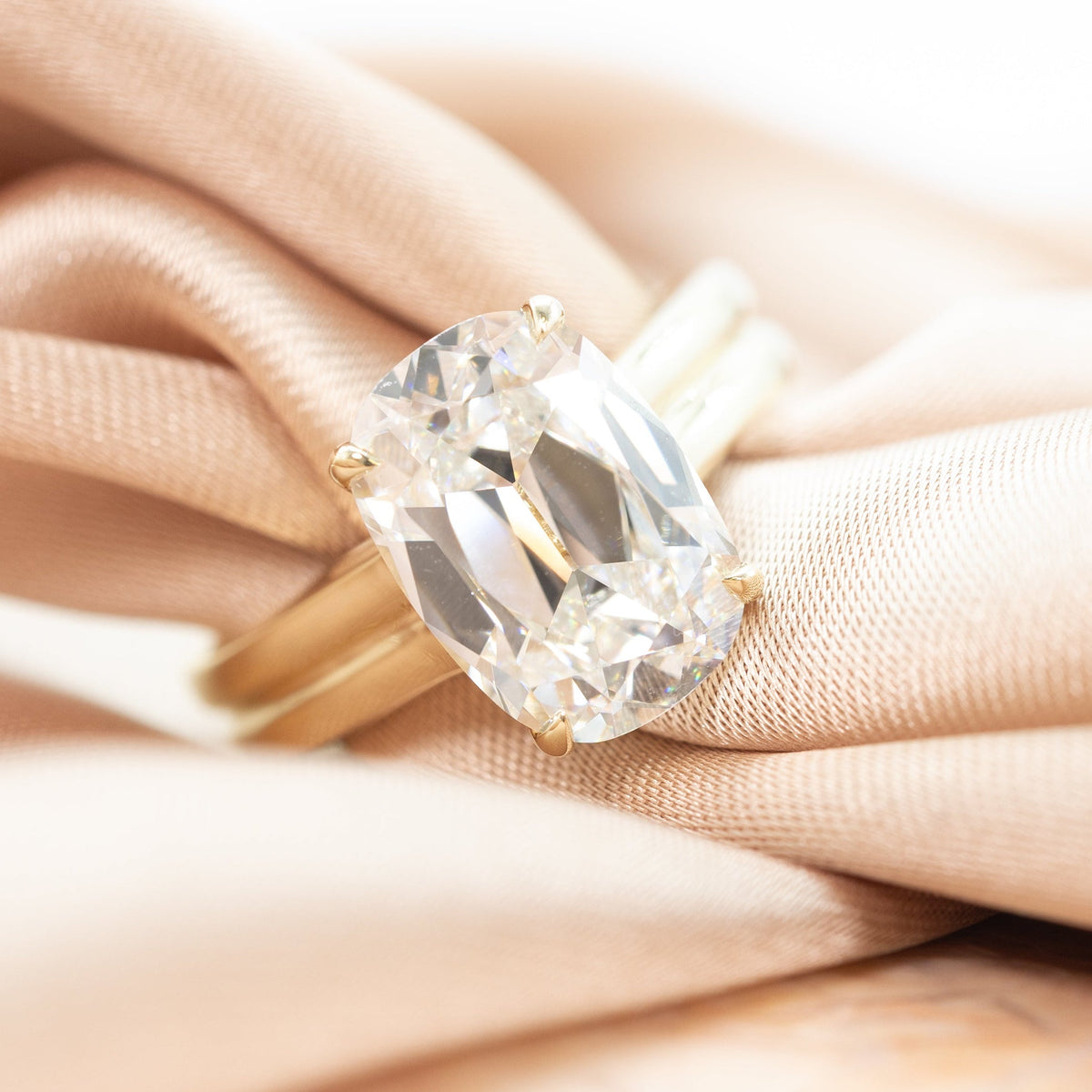 a yellow gold old mine cut engagement ring with a double ribbed band laying on a pink fabric with marble.