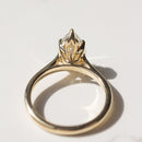 The back profile of a yellow gold engagement ring with a floral inspired tulip basket laying on a white marble backdrop.