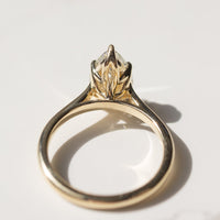 The back profile of a yellow gold engagement ring with a floral inspired tulip basket laying on a white marble backdrop.