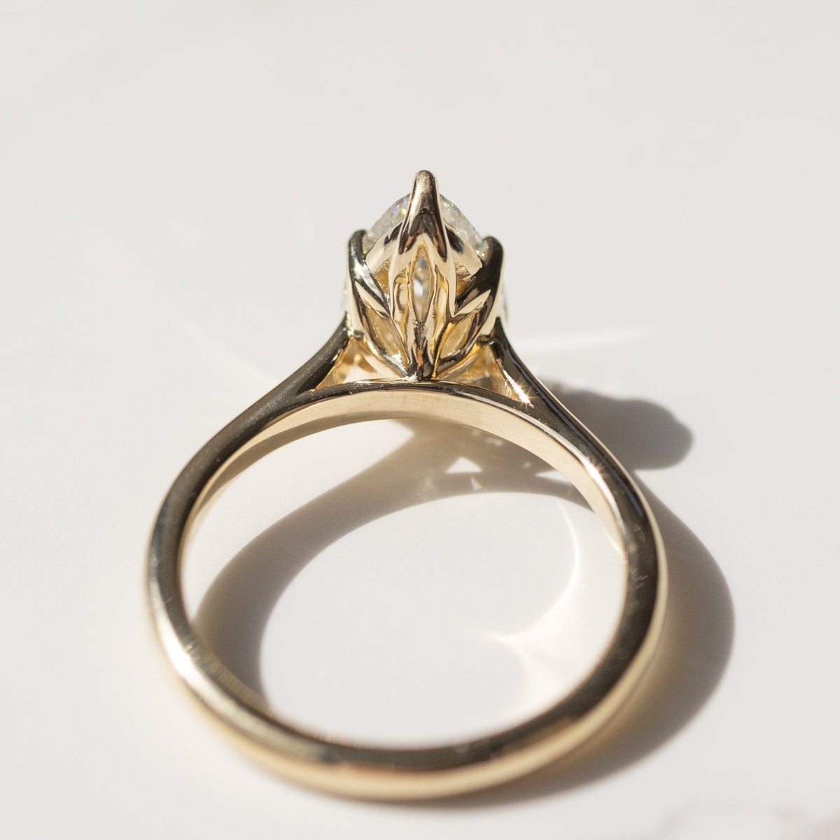 The back profile of a yellow gold engagement ring with a floral inspired tulip basket laying on a white marble backdrop.