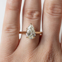 A pear cut diamond engagement ring in a yellow gold setting shown on a left ring finger along a white backdrop.