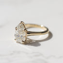 A pear cut diamond engagement ring sitting on a white marble backdrop with soft grey shadows.
