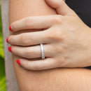 A woman holding her arm. She has bright red nail polish and a white gold diamond band on her left ring finger with dainty emerald cut diamonds.