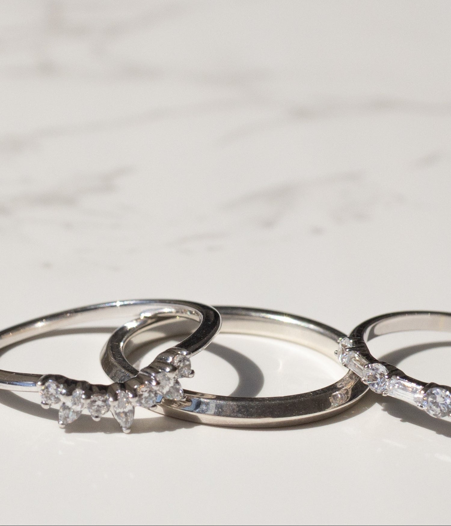 Three silver rings with diamond accents arranged on a light marble surface.