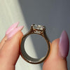 Fingers with pink nail polish holding a chunky gold engagement ring setting and showing its side profile
