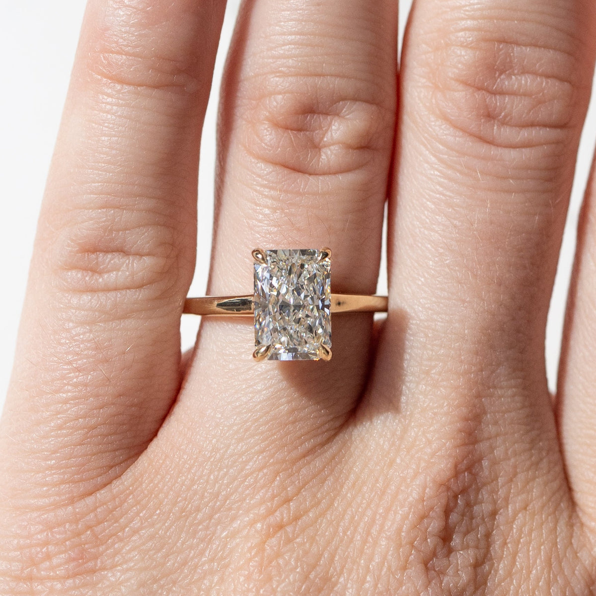 An on-hand shot of a large rectangular radiant cut diamond engagement ring in a yellow gold setting. 