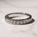 A white gold eternity ring set with clear round-cut gemstones, resting on a light marble surface.