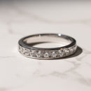 A white gold eternity ring set with clear round diamonds, resting on a light marble surface.