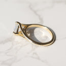 A gold ring with a asscher-cut clear diamond, resting on a white marble surface with soft shadows.