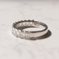 A white gold ring with emerald-cut clear diamonds, photographed on a light marble surface. The inside of the band is engraved with '14K'.