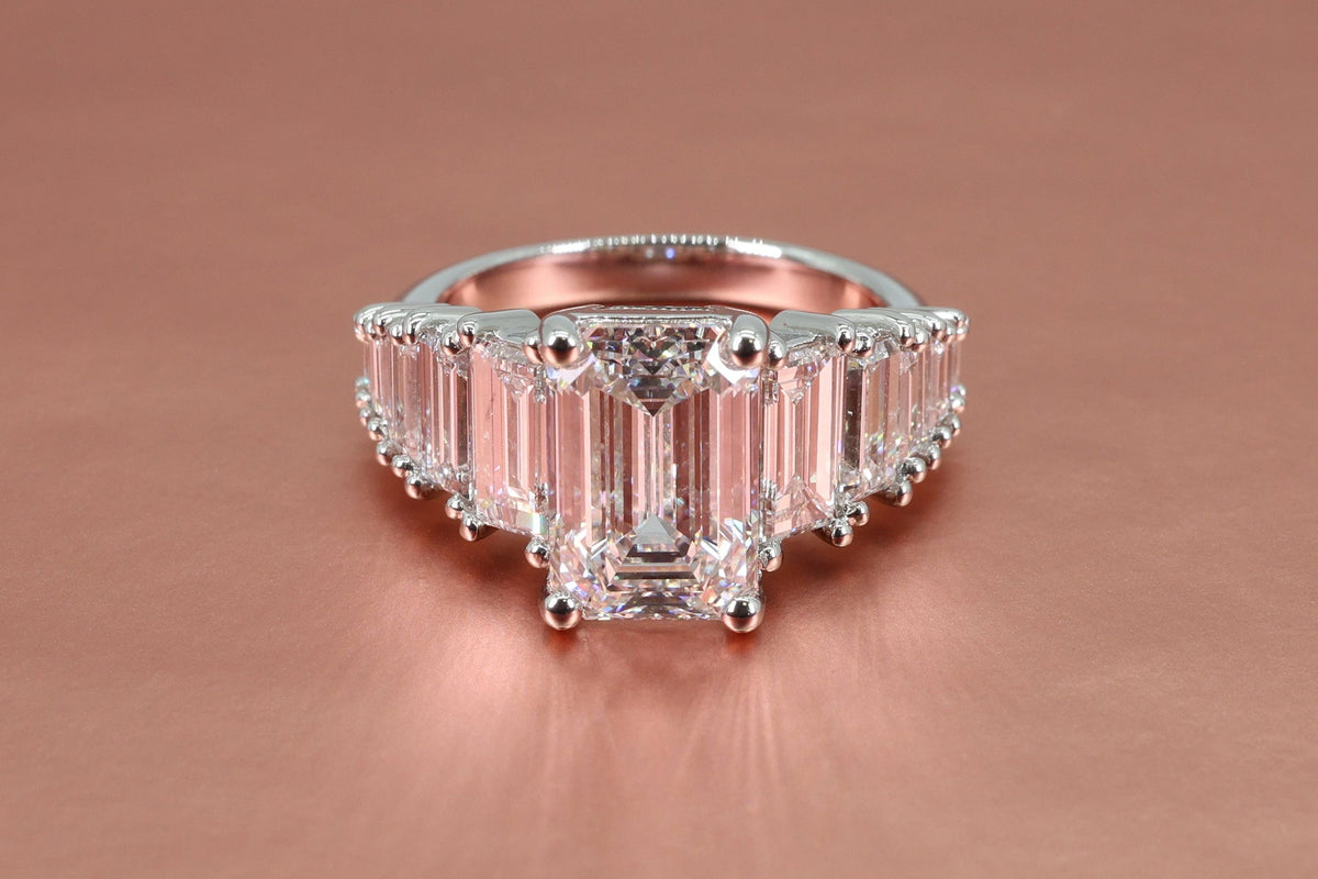 platinum engagement ring with an emerald cut diamond center sitting on a rose gold backdrop.