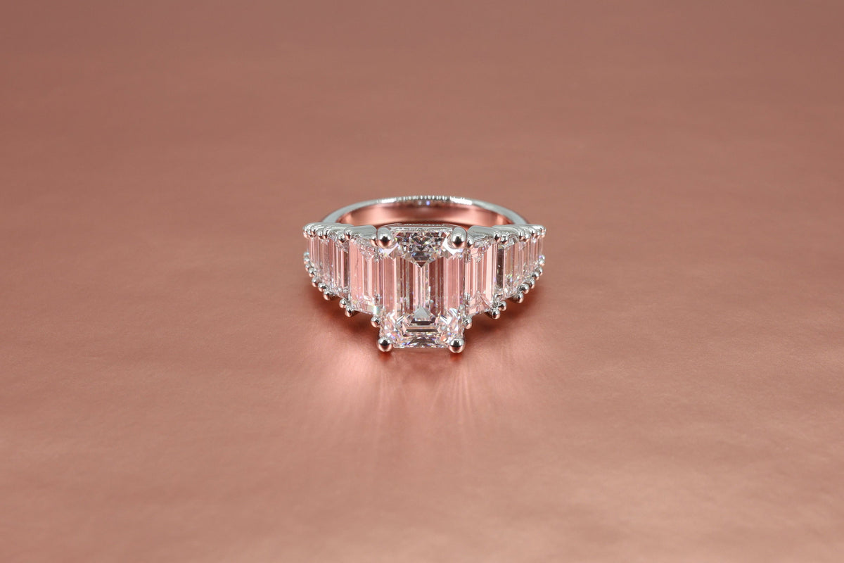 Engagement ring with emerald-cut and baguette-cut diamonds on a rose gold background