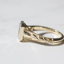 Close up tulip and milgrain detail along the side band of a yellow gold engagement ring on a white marble backdrop.