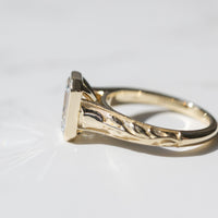 Close up tulip and milgrain detail along the side band of a yellow gold engagement ring on a white marble backdrop.