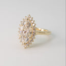 a yellow gold floral diamond halo engagement ring with a marquise center diamond on a white shadowy backdrop