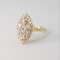 a yellow gold floral diamond halo engagement ring with a marquise center diamond on a white shadowy backdrop
