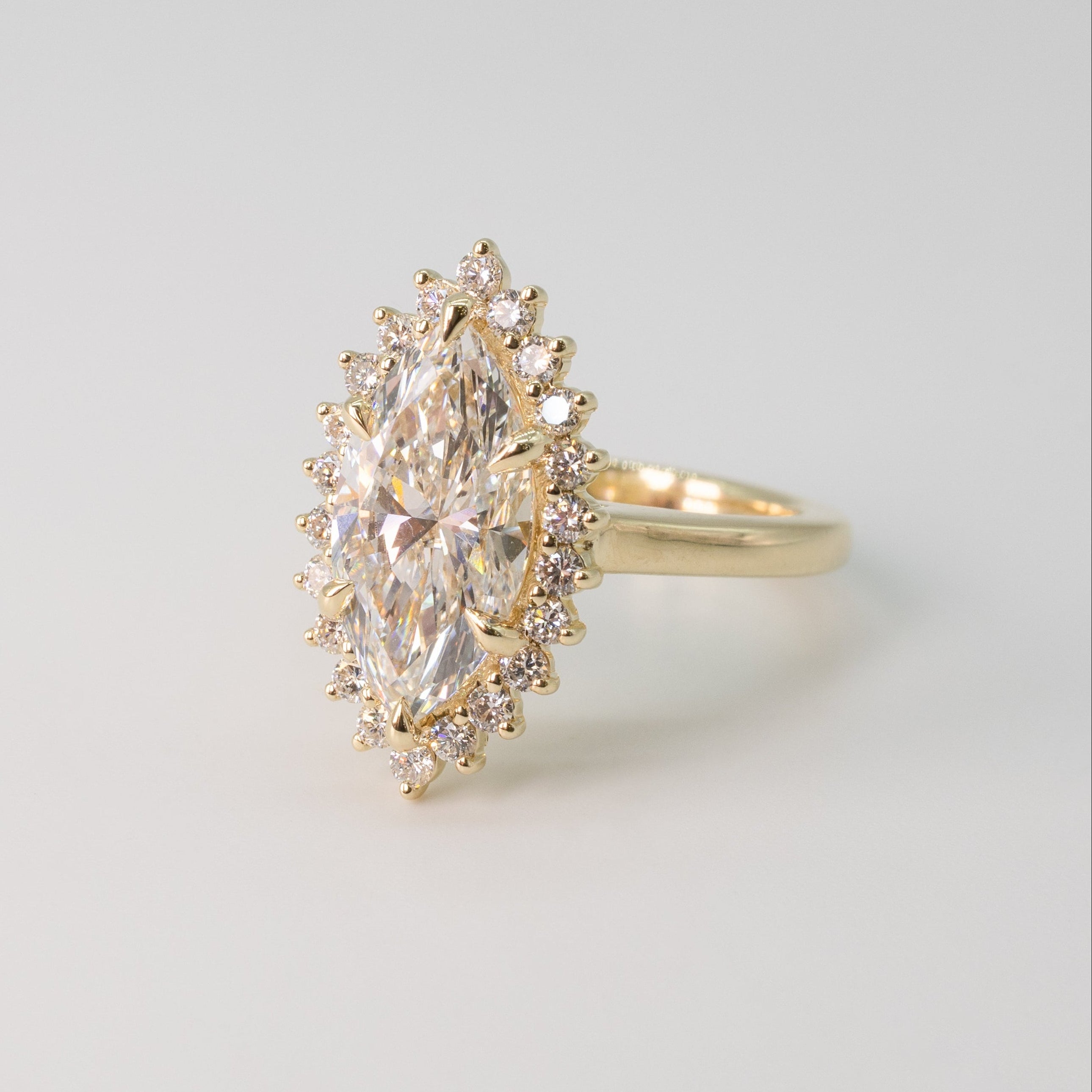 a yellow gold floral diamond halo engagement ring with a marquise center diamond on a white shadowy backdrop