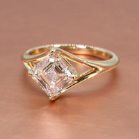 A kite-set engagement ring on a yellow gold split-shank band sitting on a rose gold backdrop