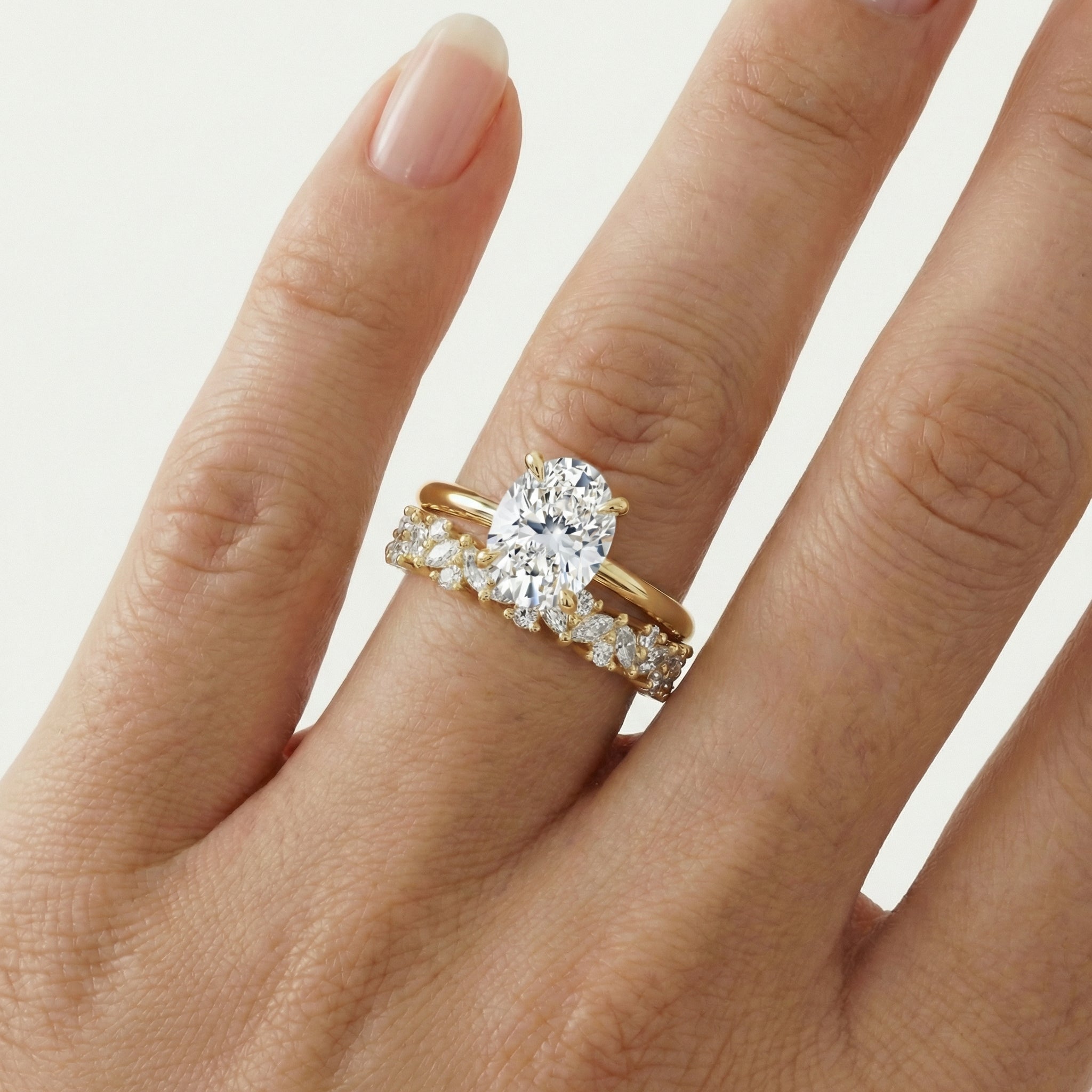 hitched women's gold diamond cluster wedding band with alternating marquise and round diamonds on model with an oval cut engagement ring