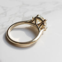 A gold ring with a large cushion diamond in a three-stone setting, resting on a white marble surface.