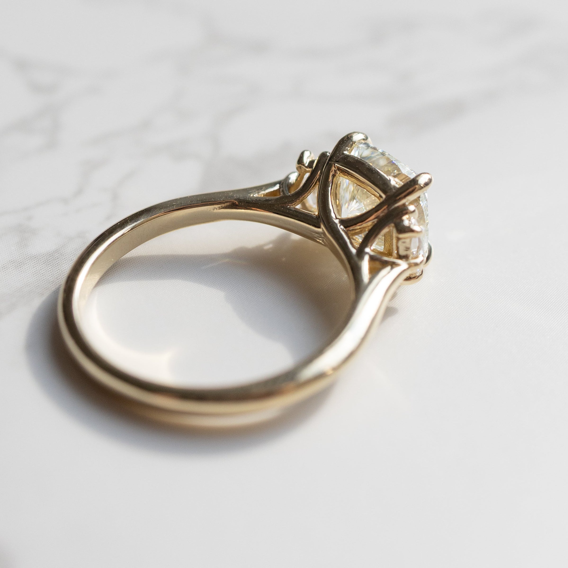 A gold ring with a large cushion diamond in a three-stone setting, resting on a white marble surface.