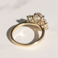 The bottom side of a yellow gold three stone engagement ring. The ring is sitting on a white marble backdrop with shadows.