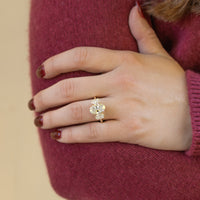 A hand being held against a fuzzy maroon sweater. On the hand is a large yellow gold engagement ring with three oval diamonds.