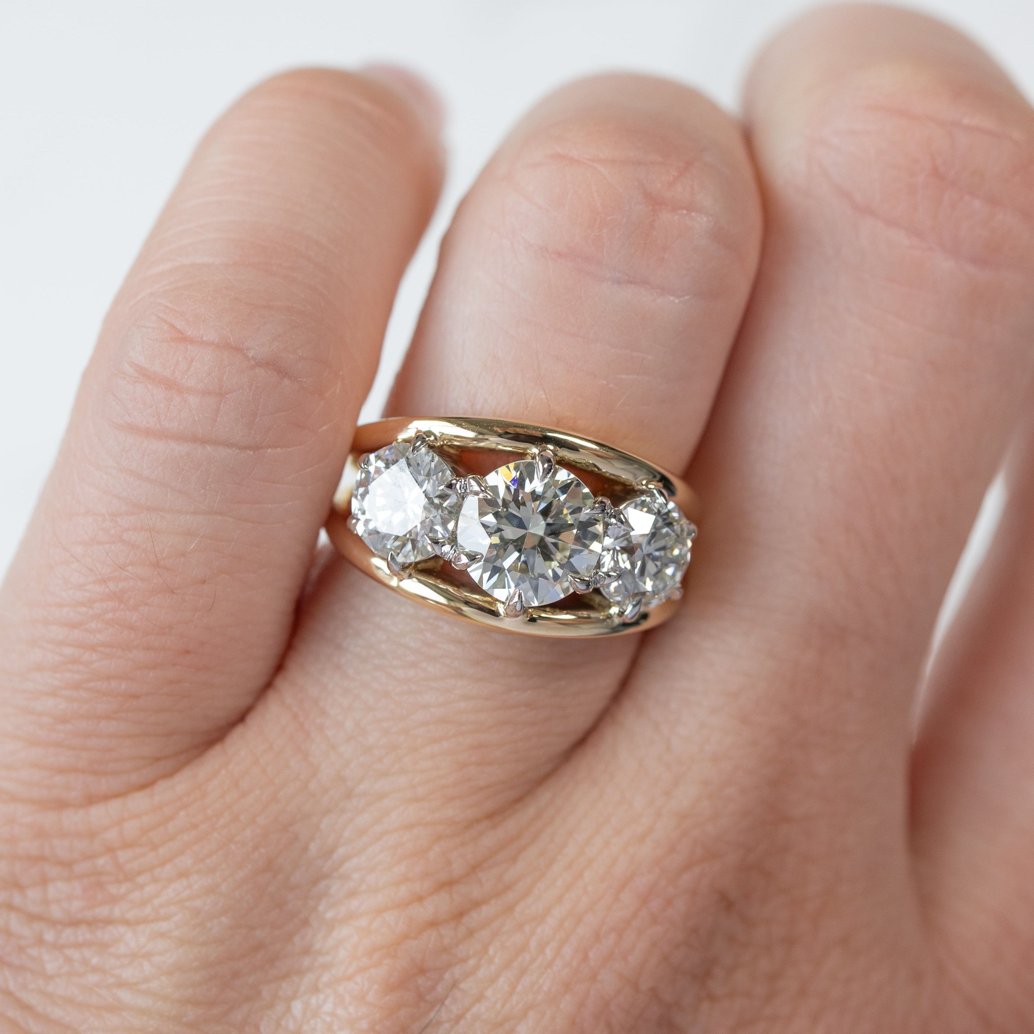 A three-stone round diamond engagement ring with a dual tone basket shown on the hand