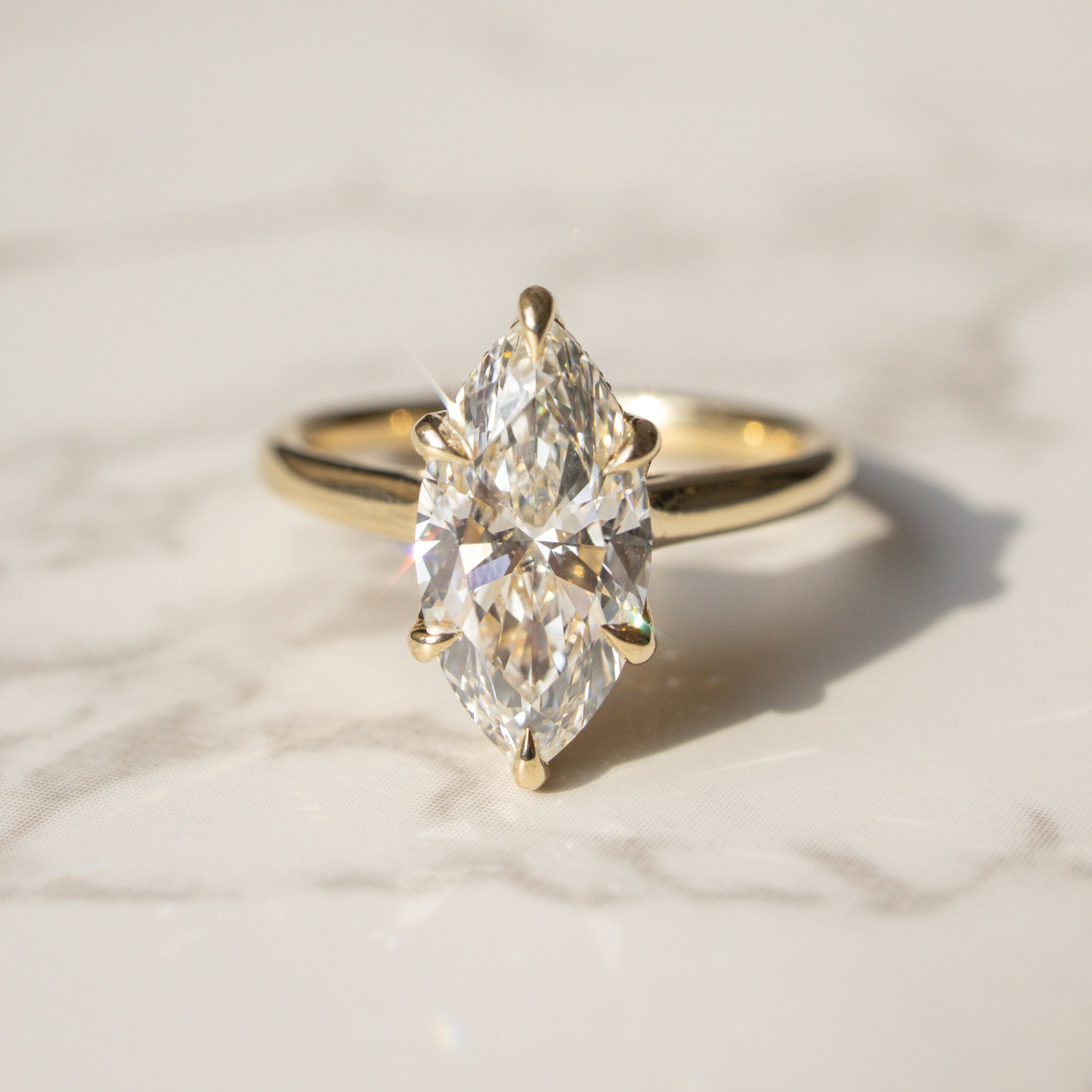 A yellow gold ring with a marquise-cut diamond solitaire setting, resting on a light marble surface.