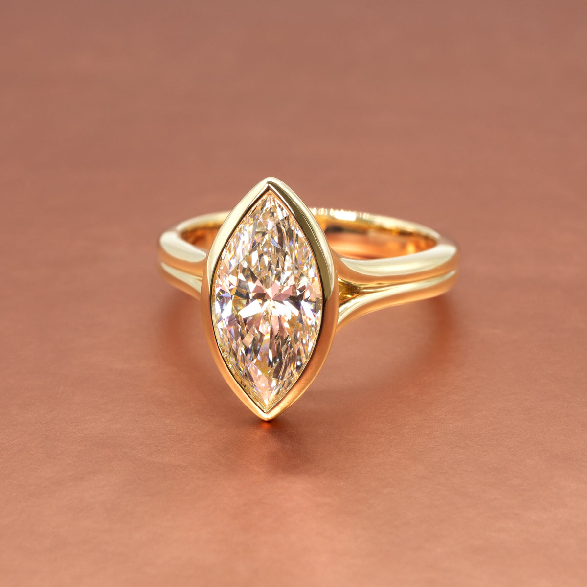 Gold ring with a marquise-shaped bezel-set diamond on a rose gold background