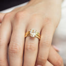 A close-up of a person's hand wearing a yellow gold ring set with an oval-cut diamond, with a matching gold flat band underneath.
